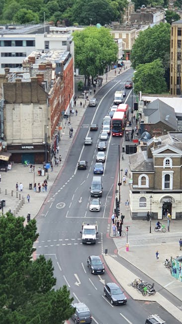 A narrow residential street in West Hampstead featuring a mix of buildings, including a brown brick structure on the left and a white building on the right with potted plants and decorative wrought ir